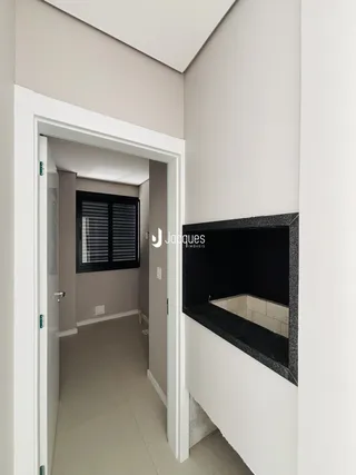 Hall de entrada com parede branca e porta de madeira em um imóvel.