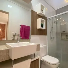 Foto de um banheiro mostrando a pia, o vaso sanitário e o box de vidro.
