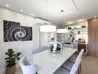 Vista de uma sala de jantar moderna com mesa de vidro e cadeiras brancas.