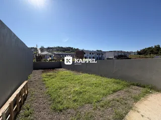 Vista externa de um terreno com grama e edificações ao fundo.
