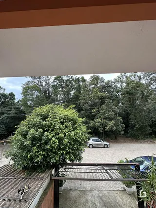 Vista externa de um quintal com árvores e uma área pavimentada.
