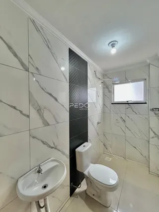 Interior de um banheiro com revestimento em mármore branco e piso claro.