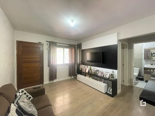 Sala de estar com piso de madeira clara e televisão na parede.