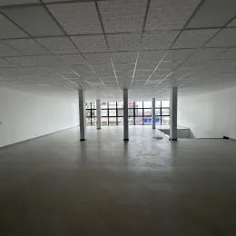 Vista interna de um espaço amplo com teto de estrutura exposta e piso de concreto.