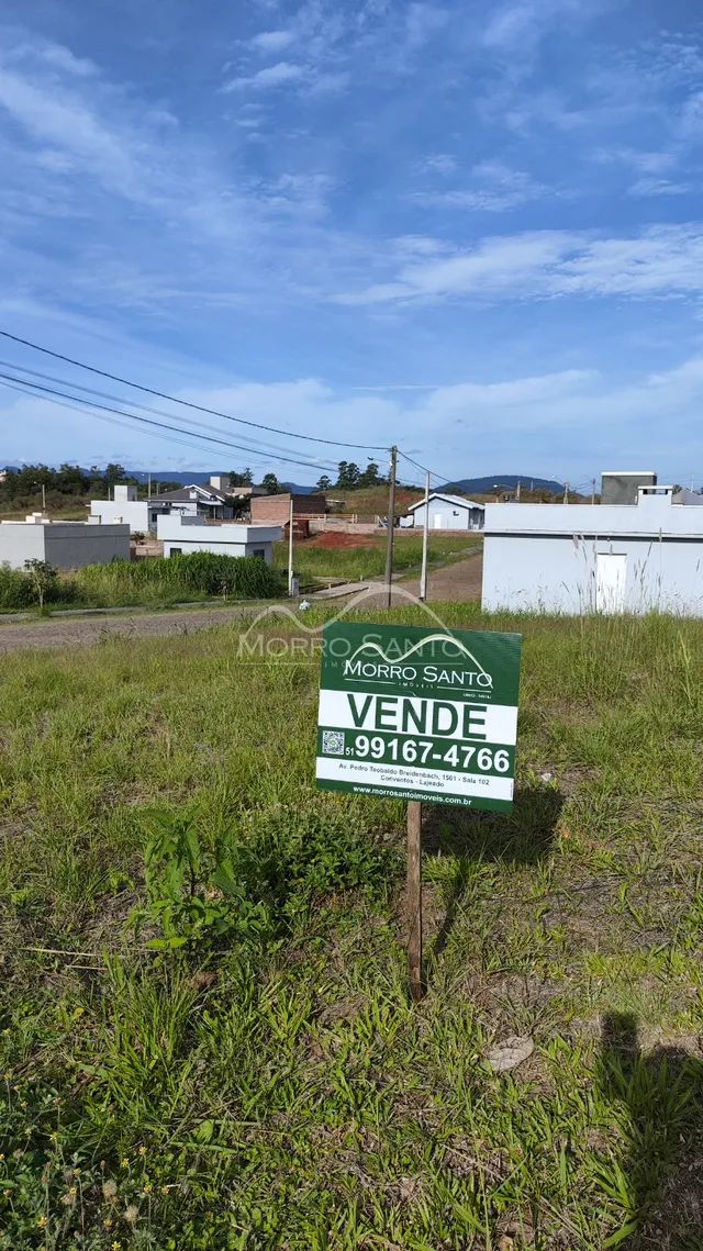 Vista externa de um terreno com vegetação alta e uma placa de venda.