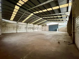Interior de um grande espaço industrial com teto metálico e paredes de tijolo.