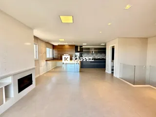 A foto mostra uma sala de estar ampla com lareira e cozinha integrada.