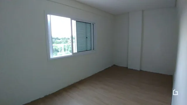 Interior de uma sala com paredes brancas e piso de madeira.