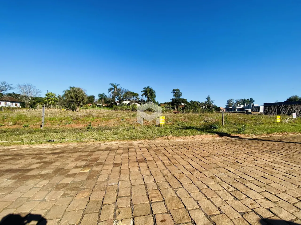 Vista externa de uma propriedade com terreno gramado e pavimentação de tijolos.