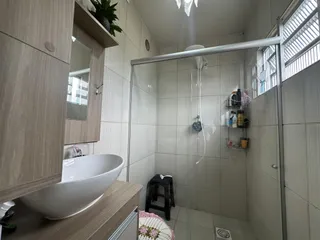 Foto interna de um banheiro com box de vidro e revestimento cerâmico.