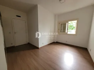 Vista interna de uma sala com piso de madeira e paredes brancas.