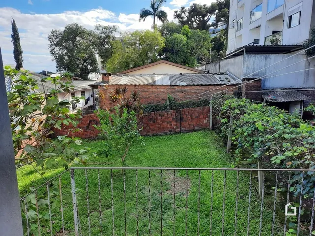 Vista externa de um quintal com muro de tijolos e vegetação.