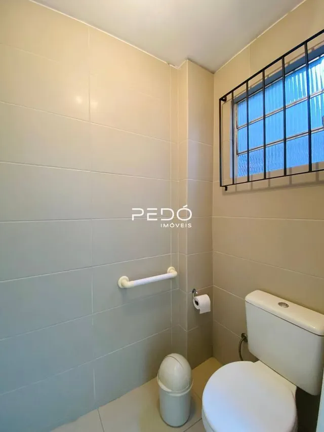 Foto interna de um banheiro com azulejos brancos e janela.