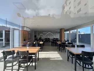 Vista de um espaço de jantar com mesas de madeira e grandes portas de vidro.