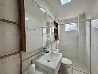 Banheiro com revestimento cerâmico branco e bancada de pia branca.