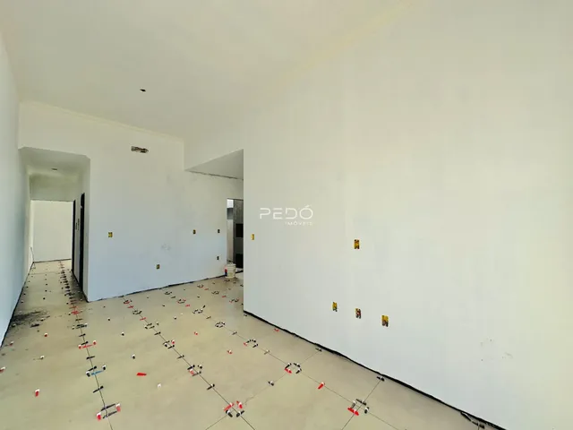 Vista interna de um ambiente com paredes brancas e piso em obra.