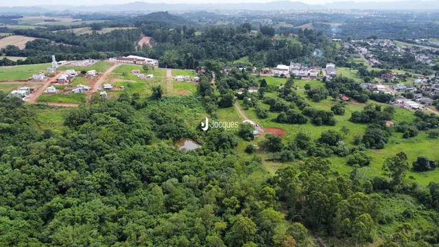 Vista aérea de uma área de mata e campos com algumas construções no meio.