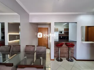 Vista de uma sala de jantar com mesa de vidro e cadeiras estofadas.