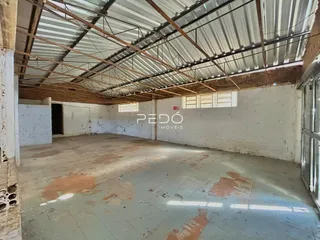 Interior de um espaço amplo com estrutura de telhado exposta e piso desgastado.