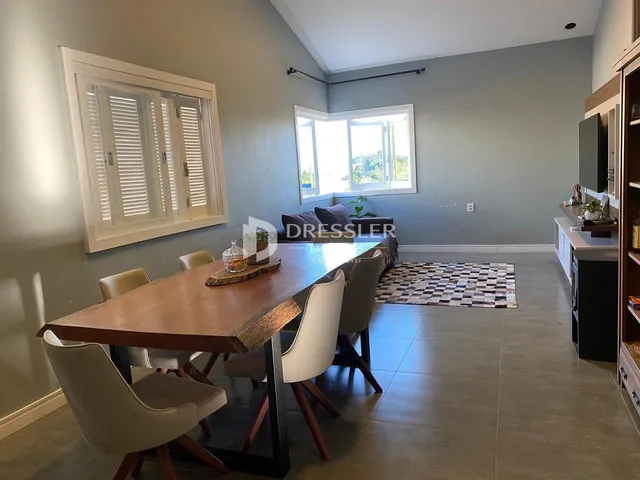 Uma sala de jantar com mesa de madeira e grandes janelas.