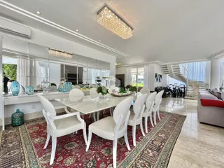 Sala de jantar ampla com mesa e cadeiras brancas em um ambiente iluminado.