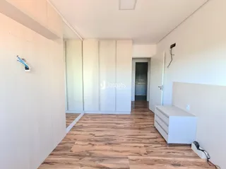 Vista interna de um ambiente com paredes brancas e piso de madeira clara.