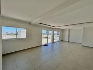 Sala de estar ampla com piso de cerâmica clara e grandes janelas.