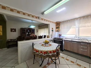 A sala de estar exibe móveis de madeira e uma janela com cortinas brancas.