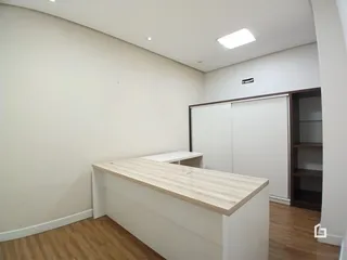 Ambiente interno de uma sala com paredes brancas e piso de madeira clara.