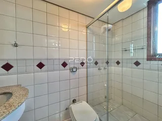Interior de um banheiro com revestimento cerâmico branco e box de vidro.