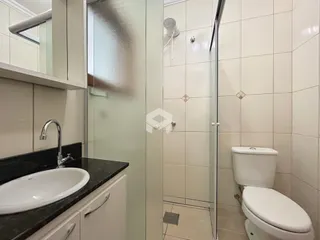 Interior de um banheiro com revestimento cerâmico e box de vidro.