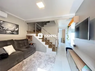 Sala de estar com sofá cinza e escadaria metálica visível.