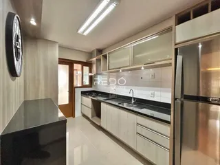 Cozinha moderna com armários brancos e bancadas escuras em um imóvel no Brasil.