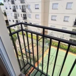 Vista da varanda com acesso a uma área externa com quadra esportiva.