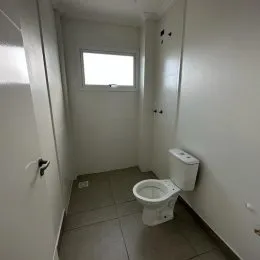 Corredor interno com paredes brancas e um vaso sanitário visível.