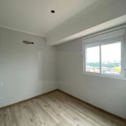Foto interna de um quarto com piso de madeira clara e janela.