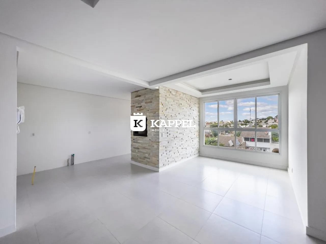 Sala ampla com piso claro e parede de pedra em um imóvel em Lajeado.