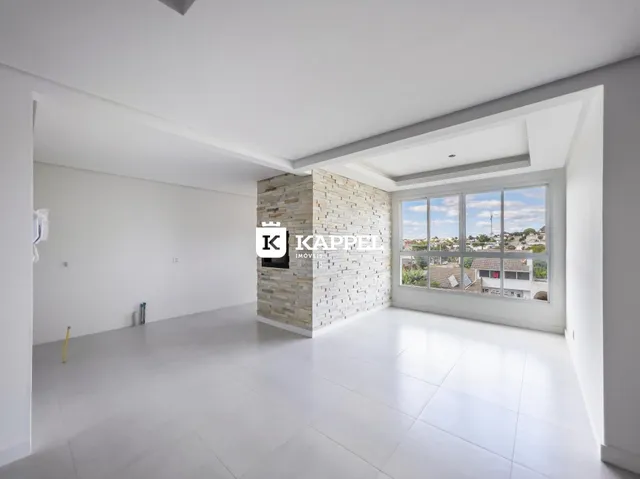 Sala ampla com piso claro e parede de pedra em um imóvel em Lajeado.