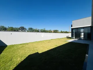 Fachada moderna de uma residência com jardim gramado e muro branco.