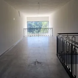 Corredor longo com piso claro e vista para uma área externa.