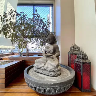 Foto de interior mostrando uma estátua de Buda perto de uma janela com vista para a natureza.