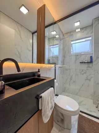 Banheiro moderno com revestimento de mármore e box de vidro.