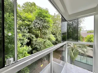 Vista externa de uma propriedade com vegetação densa e varanda de vidro.
