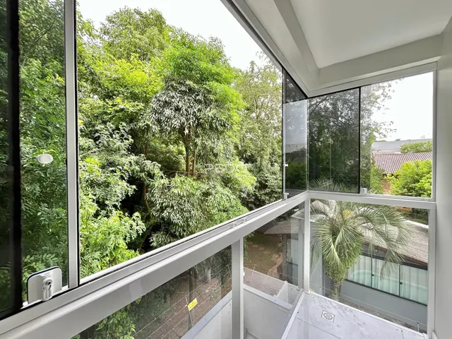 Vista externa de uma propriedade com vegetação densa e varanda de vidro.