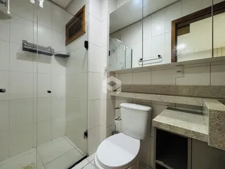 Banheiro com revestimento cerâmico e box de vidro.