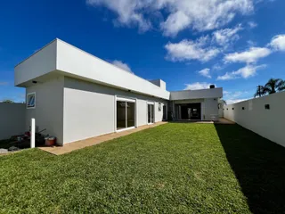 Fachada de uma casa moderna branca com gramado verde bem cuidado sob um céu azul.