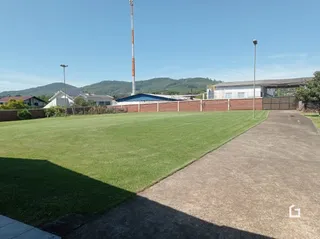 Vista externa do terreno com gramado verde e muro de tijolos.