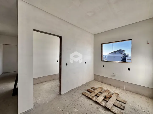 Interior de um ambiente com paredes brancas e piso de concreto cru.