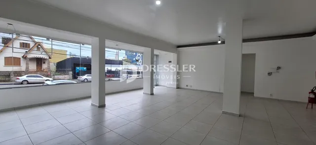 Interior de uma sala ampla com piso de cerâmica e grandes janelas.