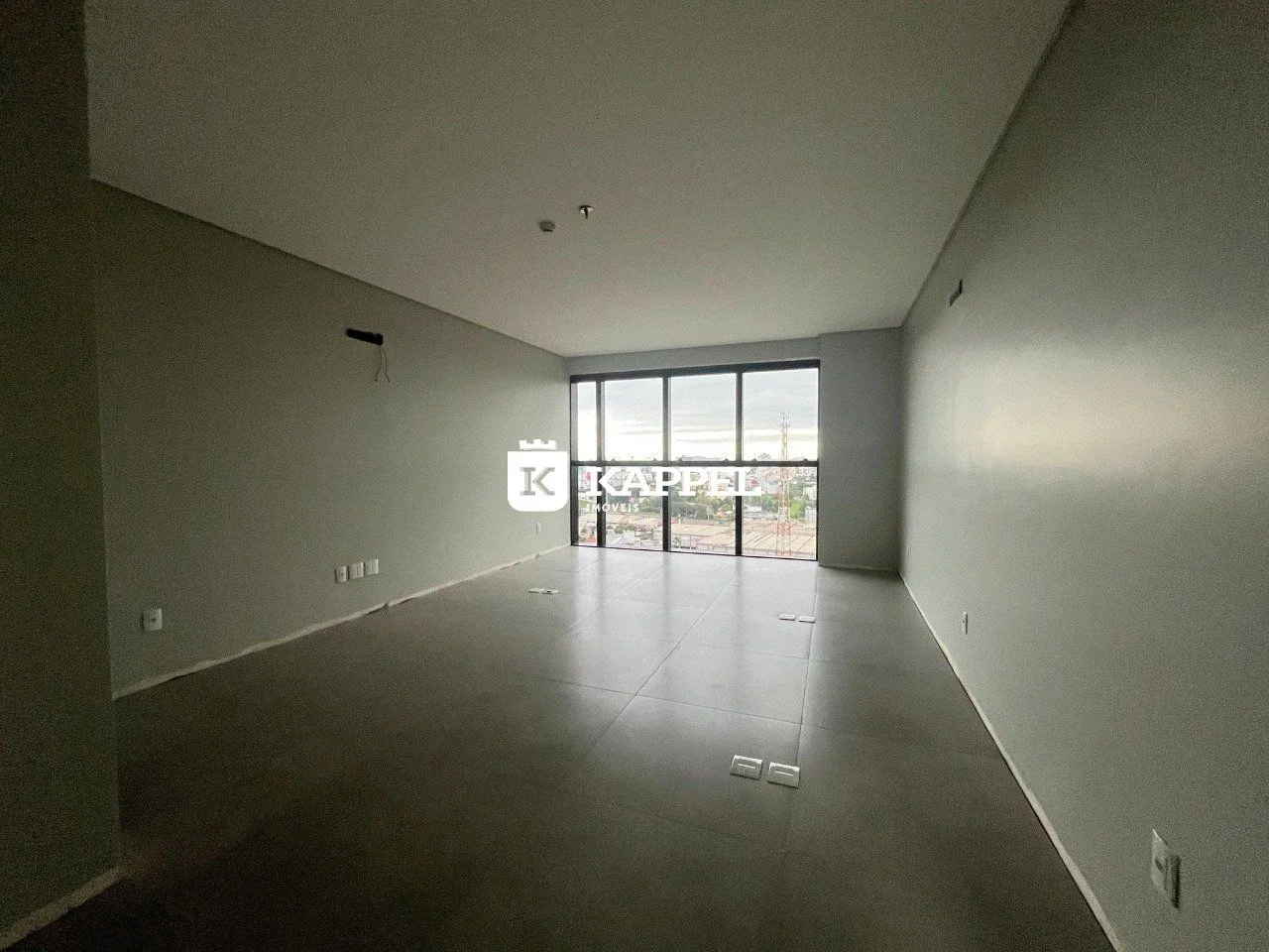 Sala ampla com piso claro e grandes janelas voltadas para o exterior.